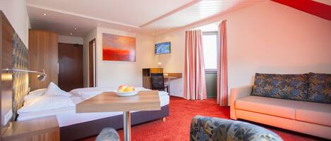 A hotel room with a bed, a desk with a laptop, a sofa, and a chair.