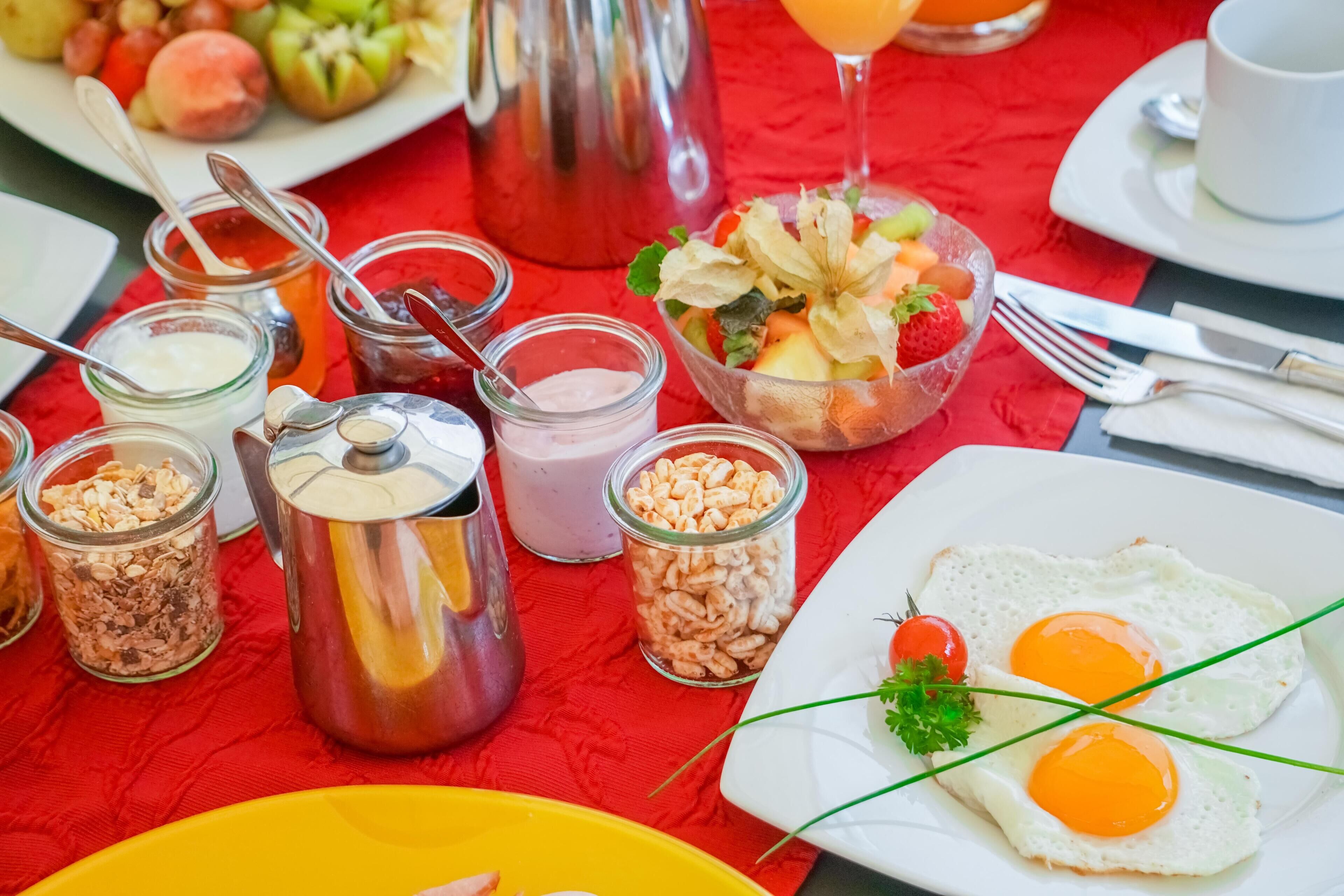 A breakfast setting with various food items and condiments on a red tablecloth.