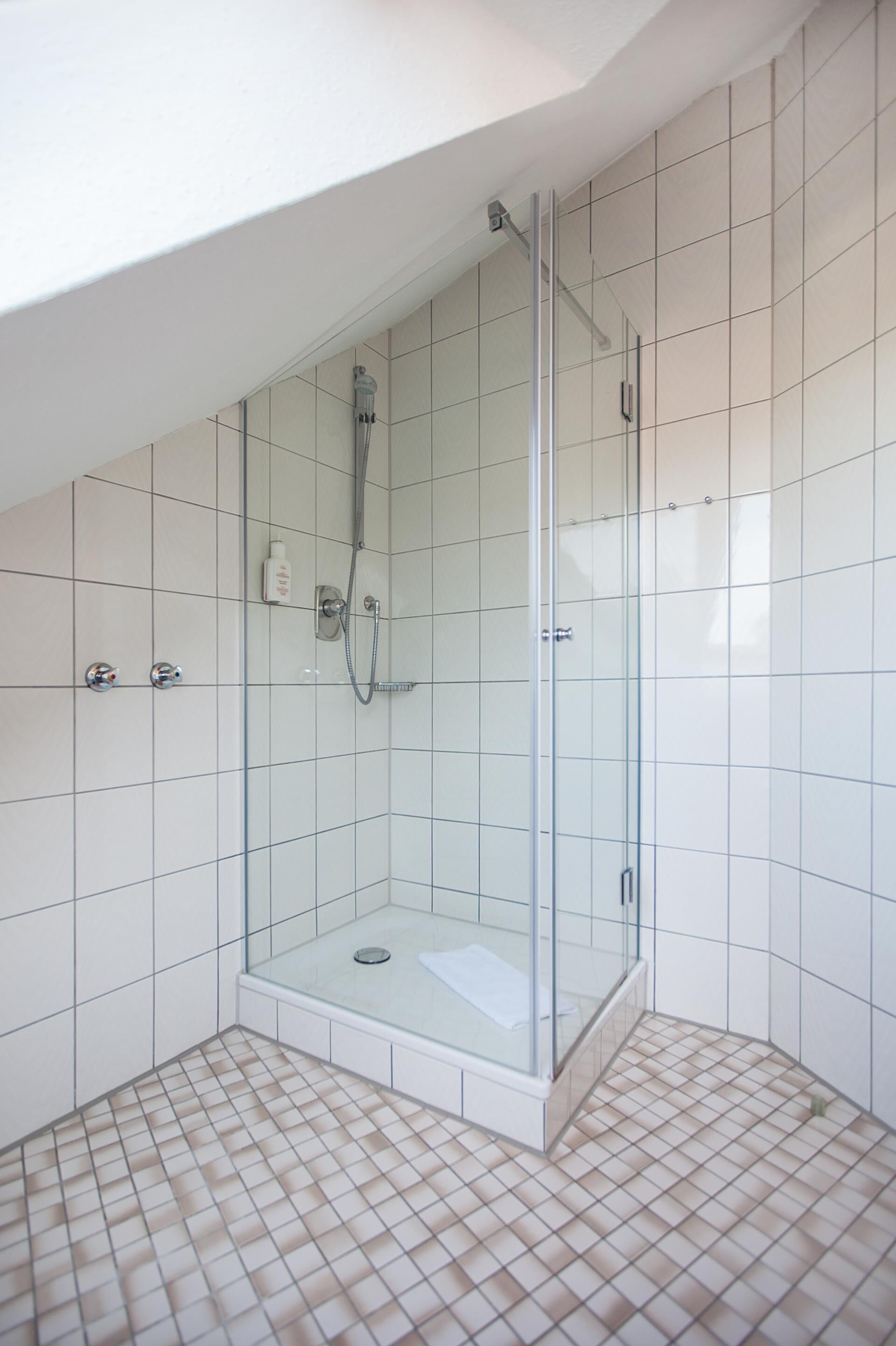 Eine begehbare Dusche mit Glastrennwand, gefliestem Boden und weißen Wänden.