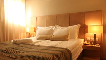 A hotel room with a large bed, two bedside lamps, a nightstand with a phone, and an air conditioning unit.