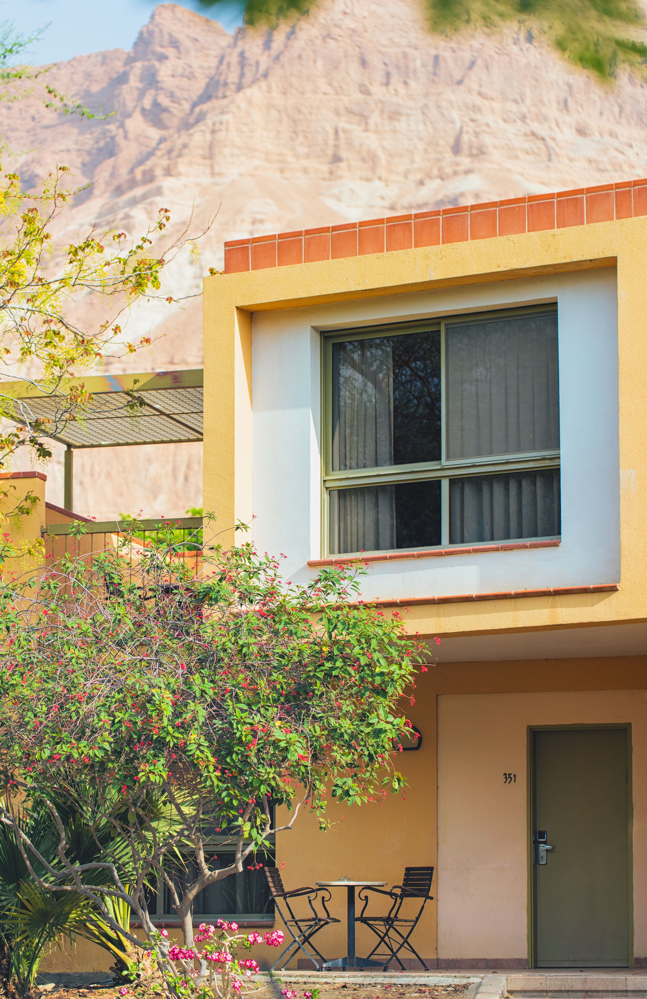 Un edificio de dos pisos con techo plano, una puerta verde y una ventana con cortina.