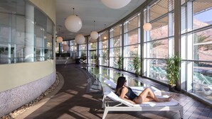 Un espace piscine intérieur baigné de lumière naturelle, avec un fauteuil de relaxation, de grandes fenêtres et des plantes en pot.