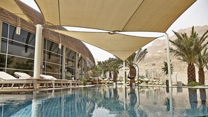 Un espace piscine agrémenté de chaises longues et de parasols, entouré de palmiers et dominé par un paysage montagneux.