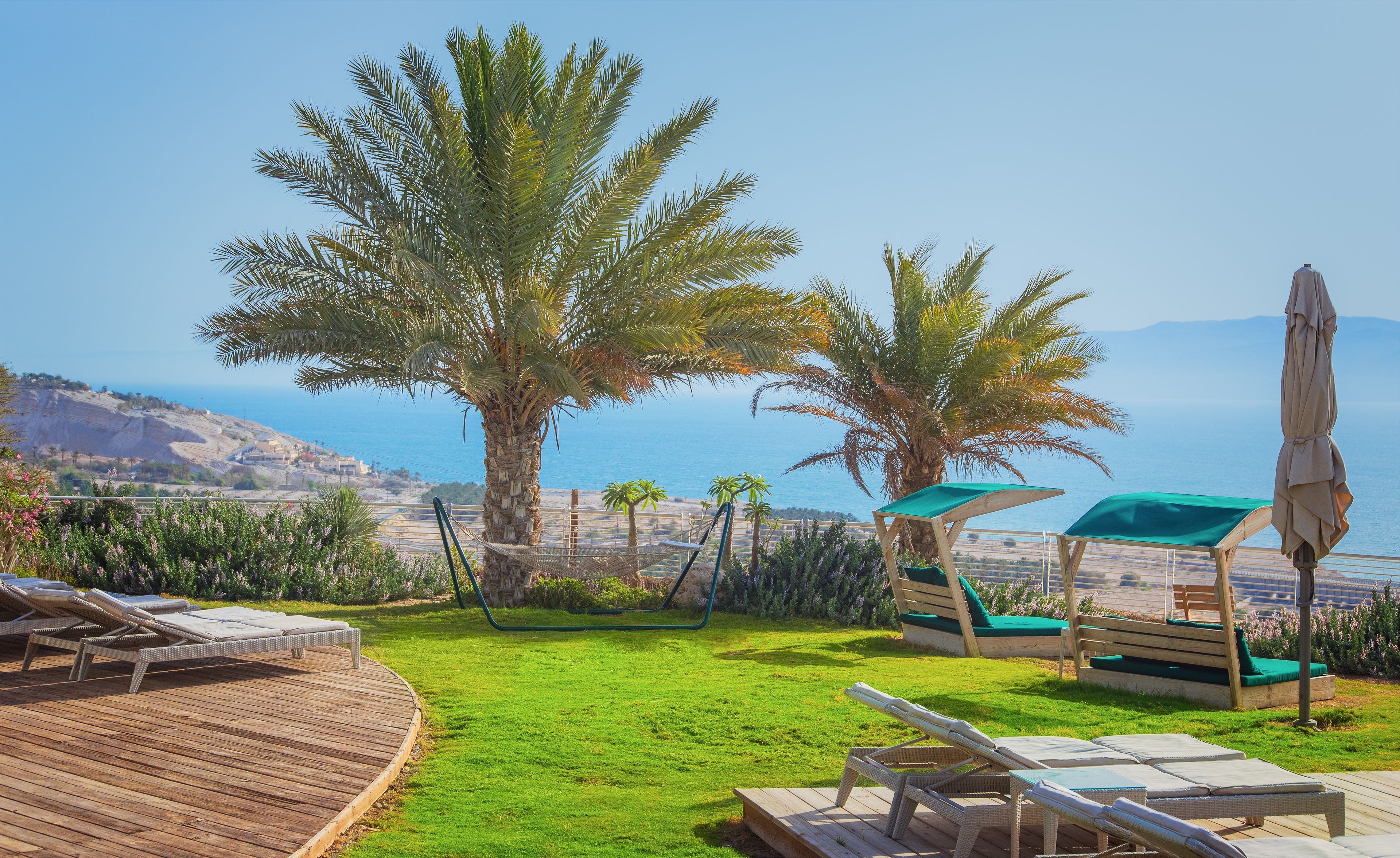 A deck with lounge chairs and a hammock overlooking a coastal landscape with palm trees and a view of the sea.