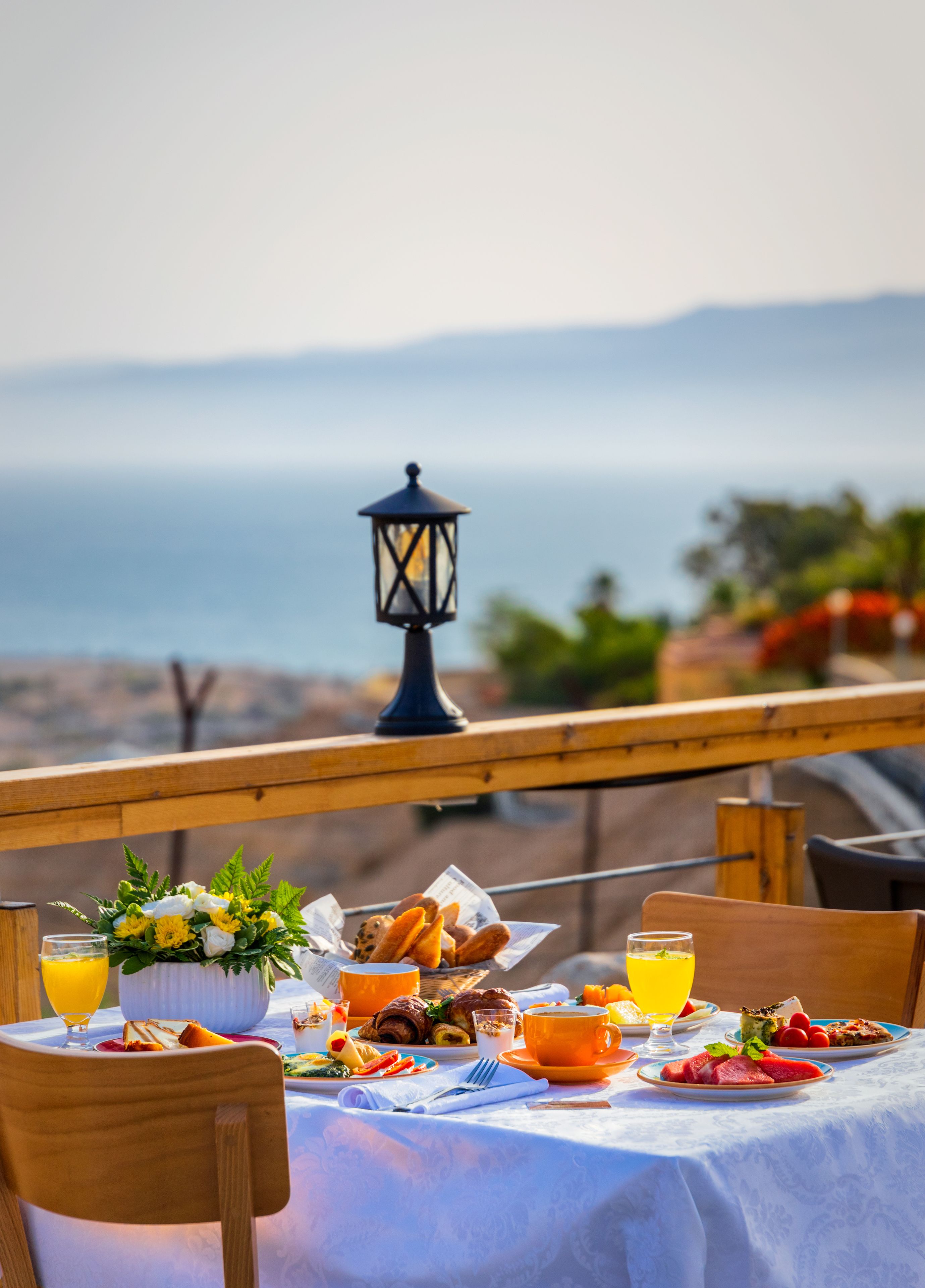Ein Tisch reichhaltig gedeckt mit Frühstücksleckereien, eine Laterne und Blick aufs Meer.
