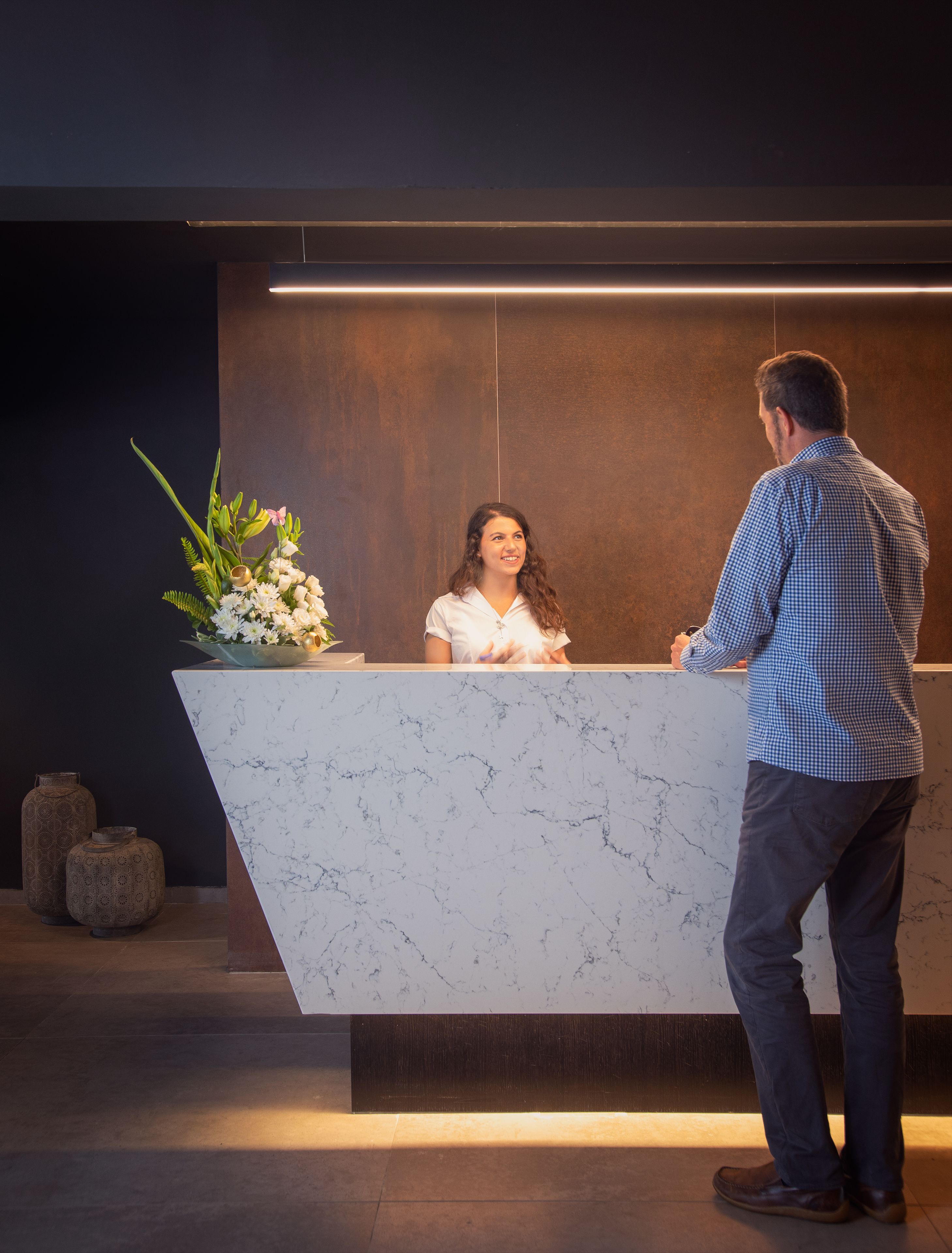 A reception desk with a marble top, a vase of flowers, and a modern wall design.