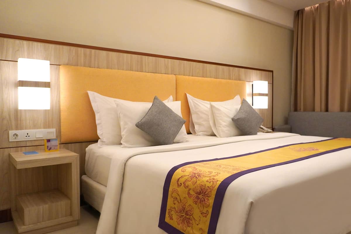 A hotel room with a large bed, two bedside tables, a nightstand, and a headboard with integrated lighting.