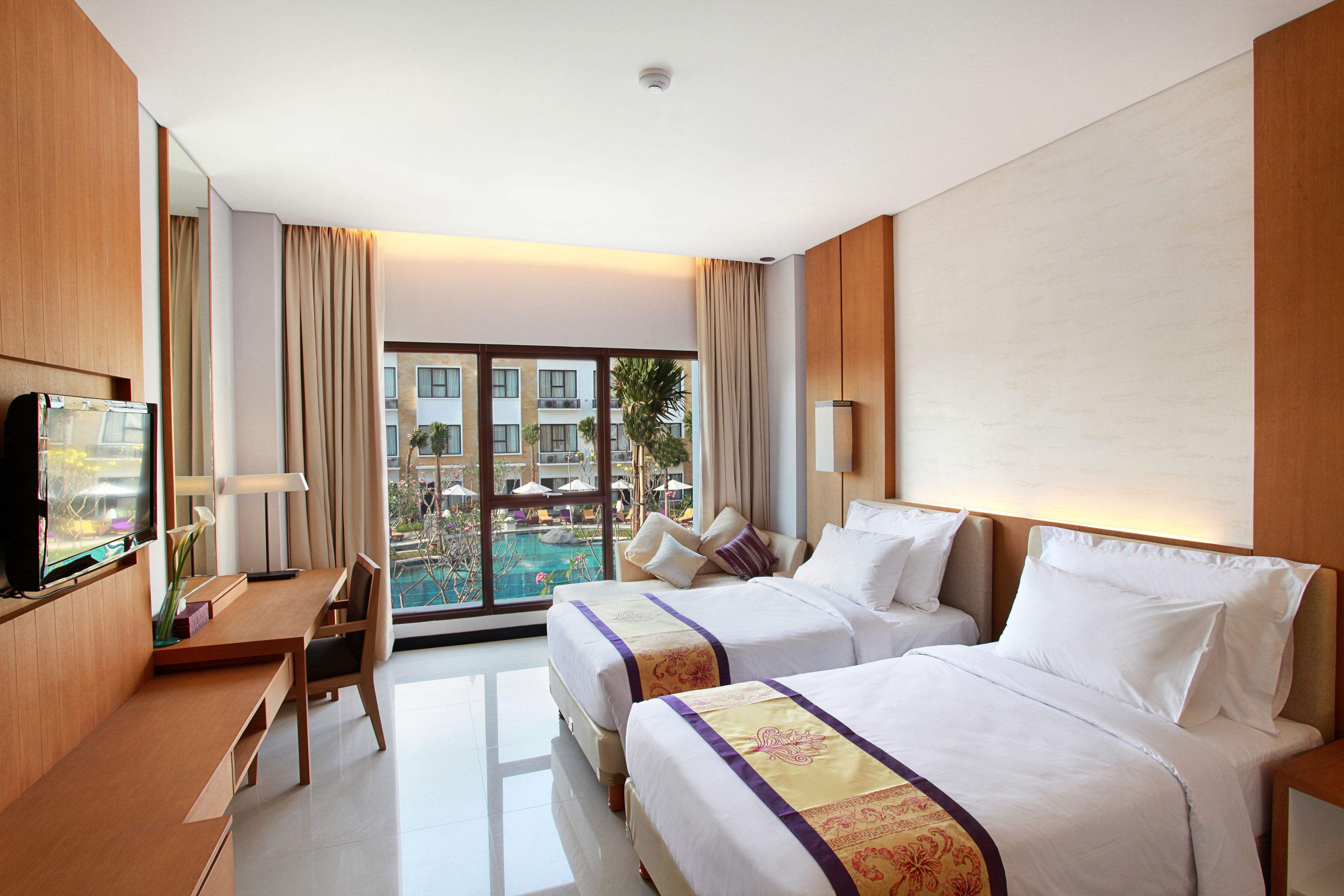 A hotel room with two beds, a desk, a TV, and a view of a swimming pool.