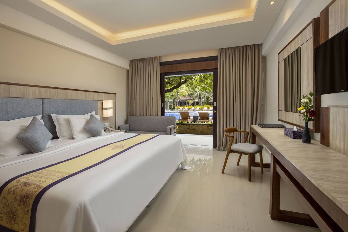 A hotel room with a large bed, a desk, a chair, and a view of a pool area.