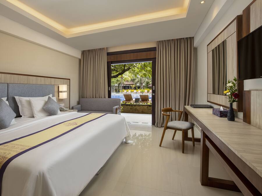 A hotel room with a large bed, a desk, a chair, and a view of a pool area.