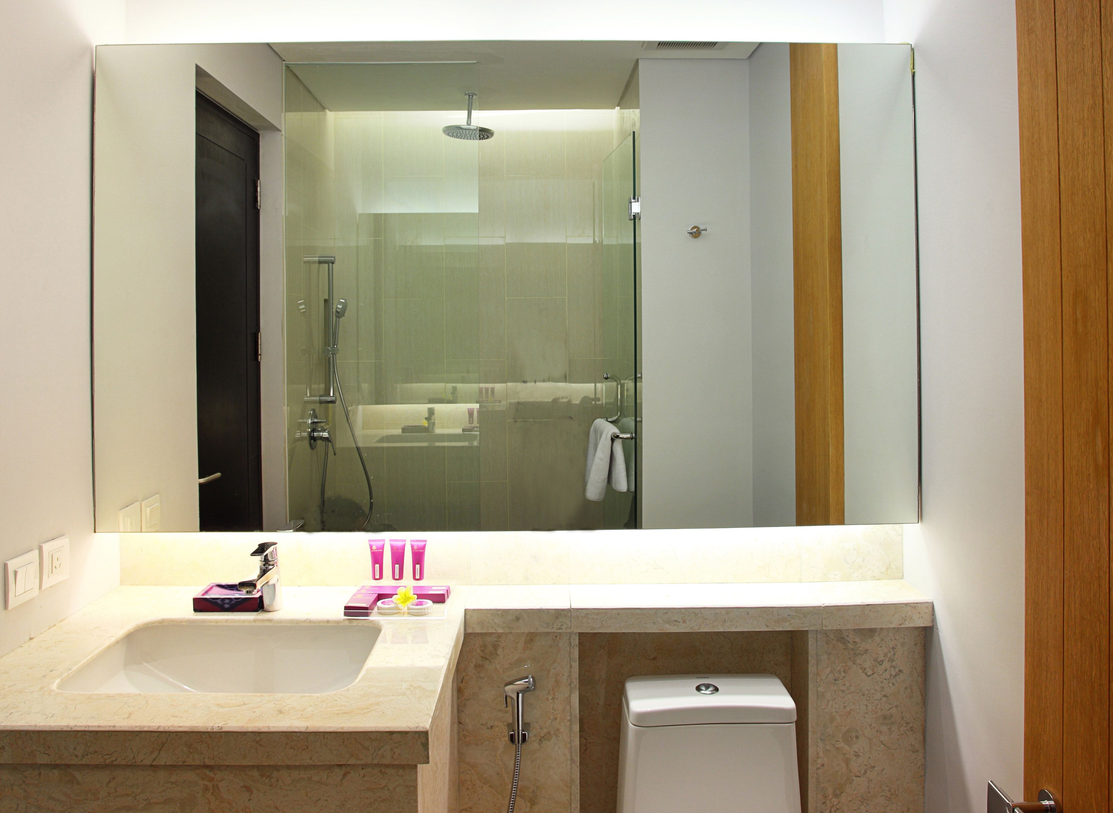 A bathroom with a large mirror, a sink, a shower, and a toilet.