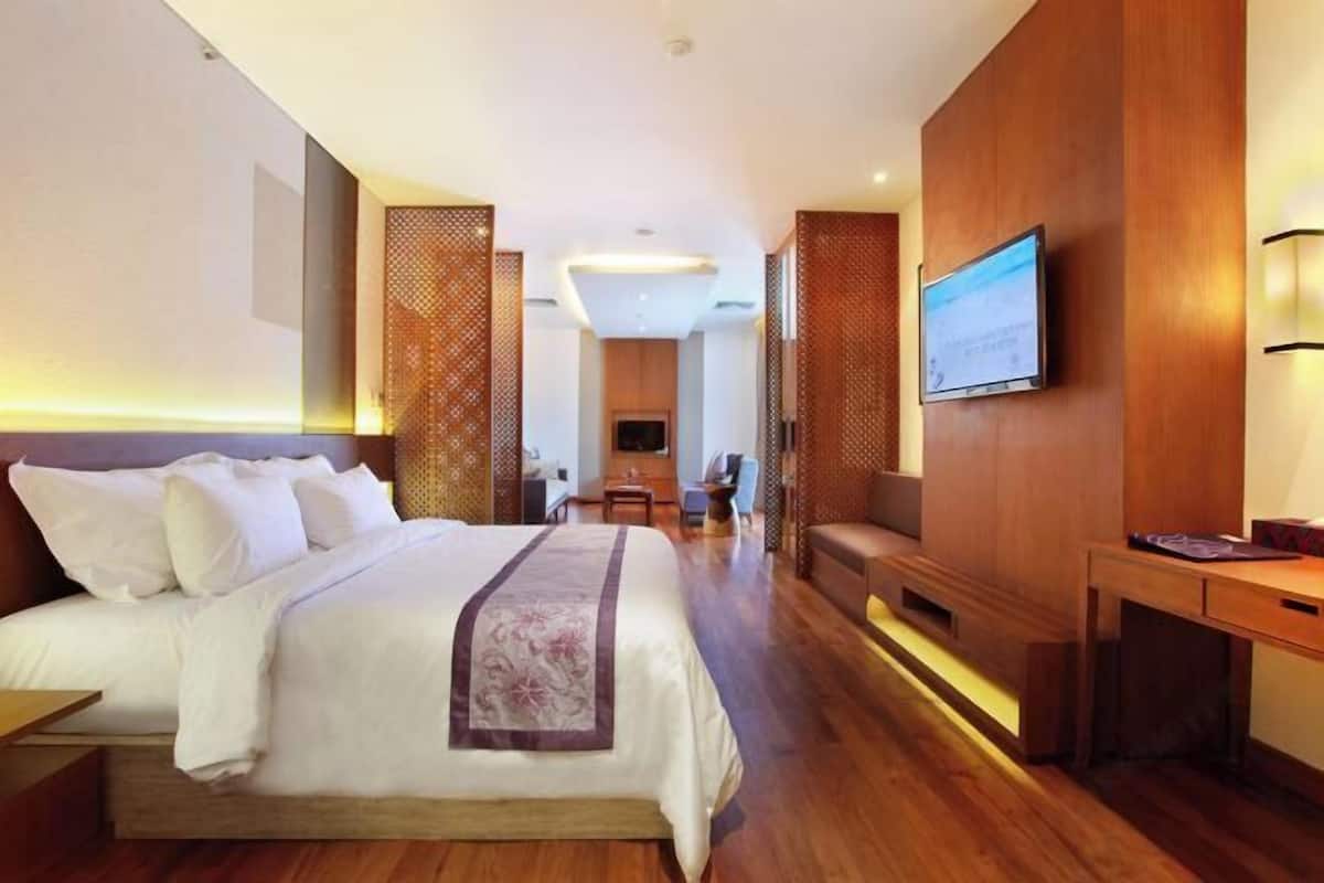 A hotel room with a bed, a desk, a TV, and a seating area.
