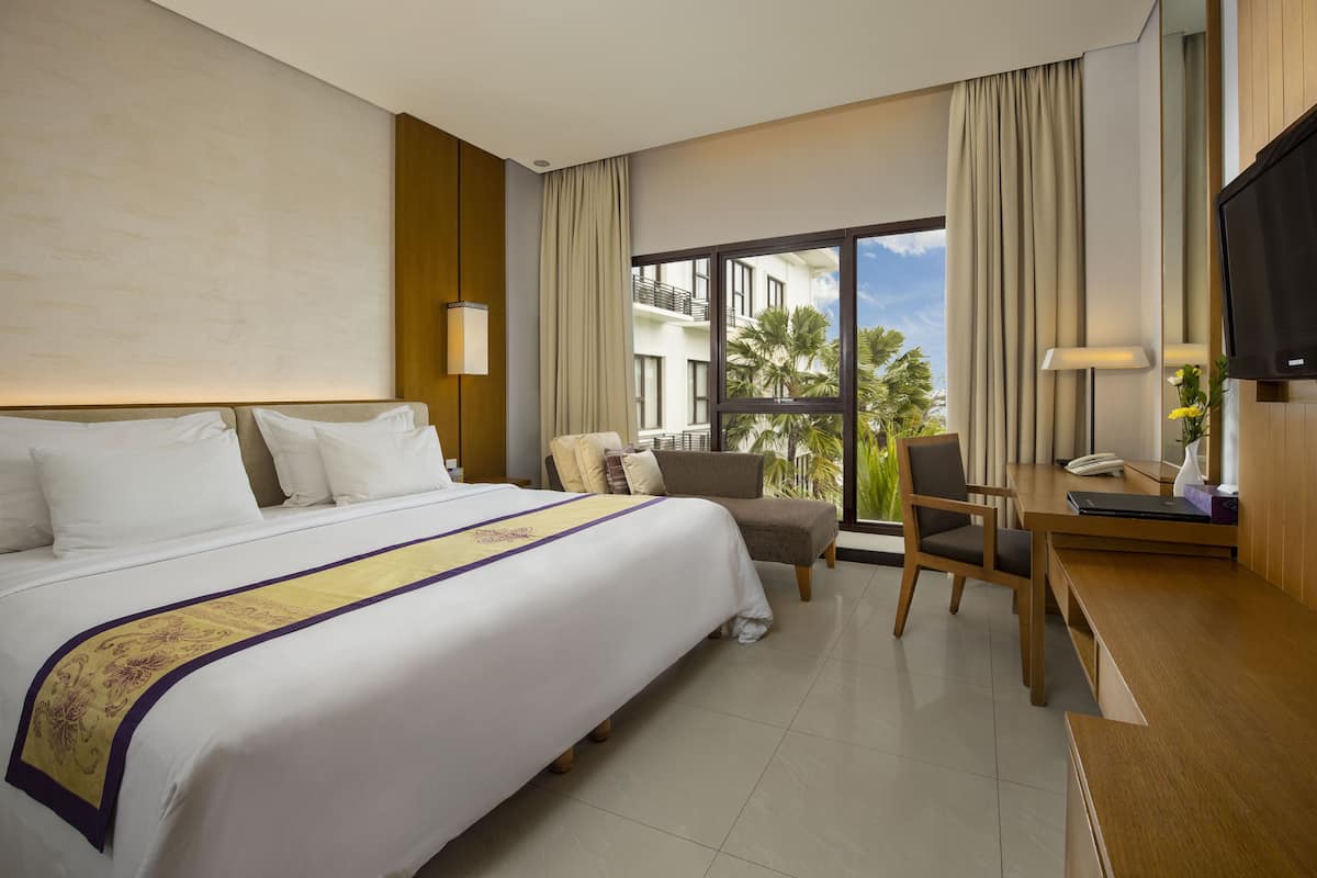 A hotel room with a large bed, a desk, a chair, and a TV.