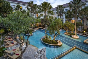 A resort pool area with multiple swimming pools, lounge chairs, and palm trees.