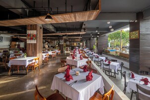A spacious restaurant with multiple tables and chairs, wooden accents, and a view of greenery outside.