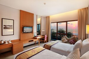 Ein Hotelzimmer mit zwei Betten, einem Schreibtisch, einem Fernseher und einem großen Fenster mit Sonnenuntergangsblick.