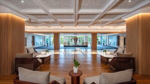 Un vestíbulo amplio con mobiliario de madera, una pieza decorativa central y grandes ventanales con vistas al exterior.