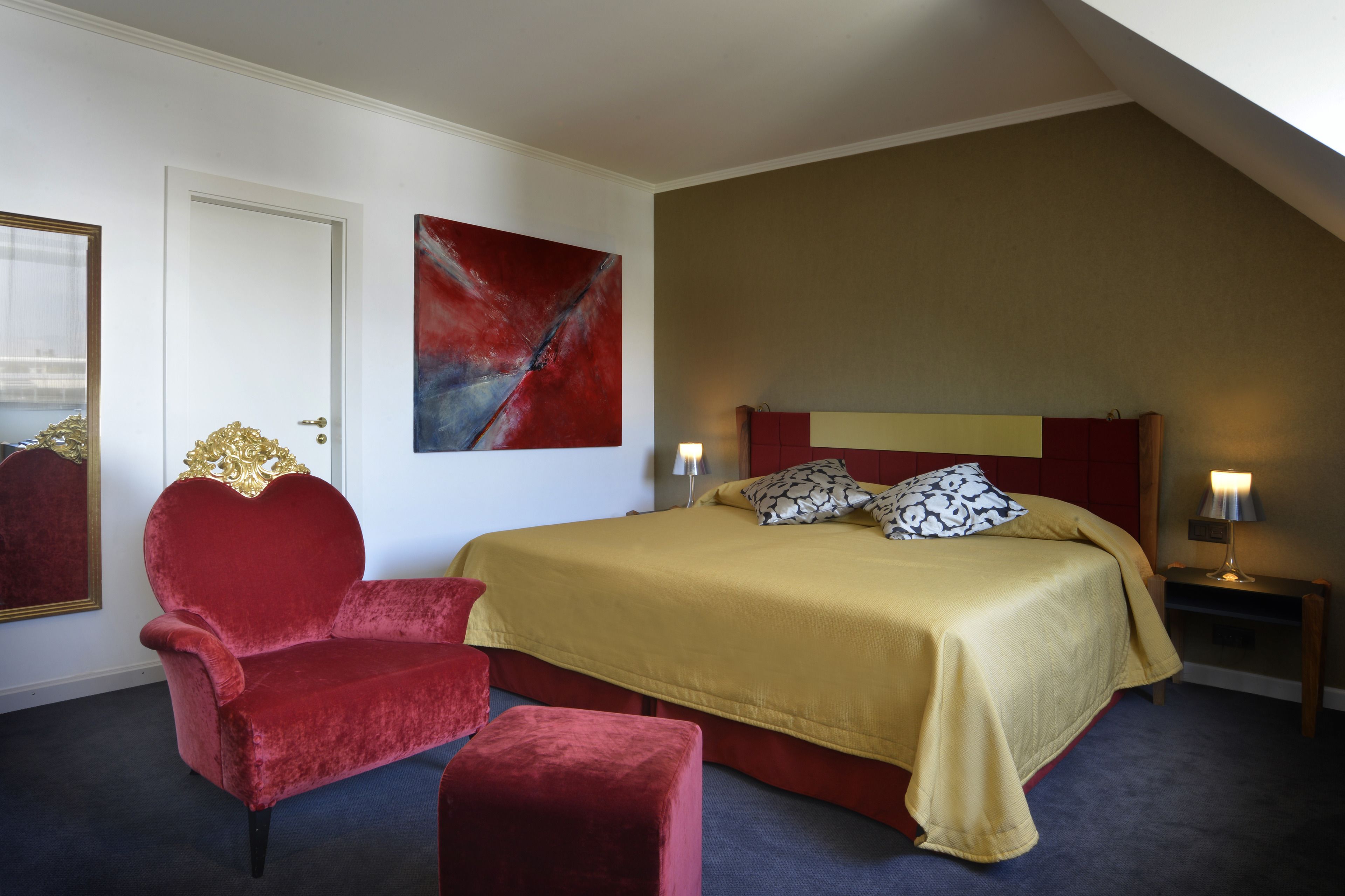 A bedroom with a large bed, a red armchair, a red ottoman, a red headboard, and a red accent wall.