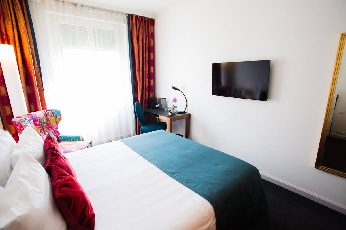 A hotel room with a bed, a desk, a chair, a TV, and a mirror.