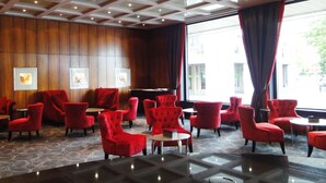 A lobby with red upholstered chairs, a piano, and framed pictures on the wall.