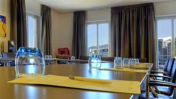 Un salón de conferencias con una mesa larga, sillas y vistas a un paisaje urbano a través de amplios ventanales.