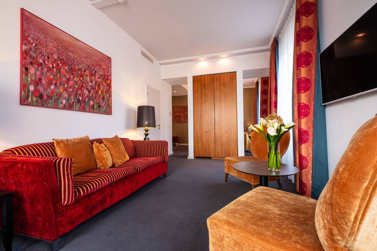 A modern living room with a red sofa, a small round table with a vase of flowers, and a large painting on the wall.