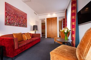 Una sala moderna con un sofá rojo, una mesita redonda con un florero y un cuadro grande en la pared.