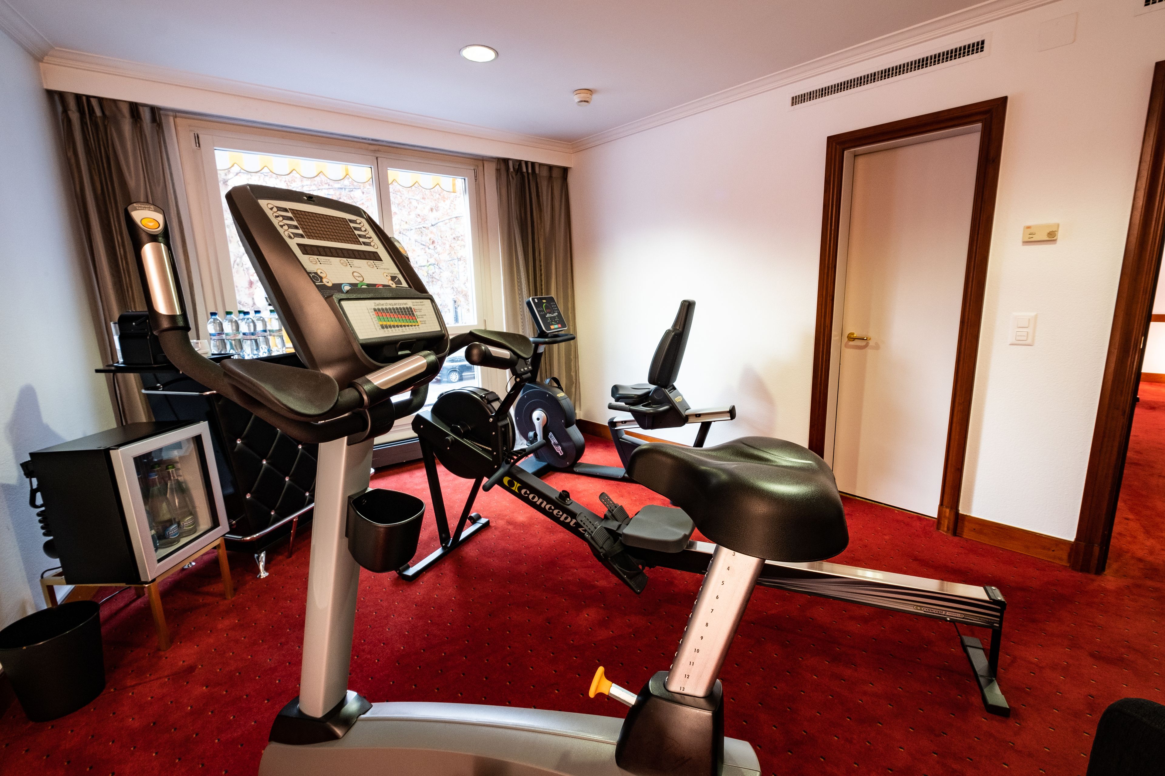 Une salle de sport à domicile équipée de matériel d’exercice, avec un tapis rouge et une porte.