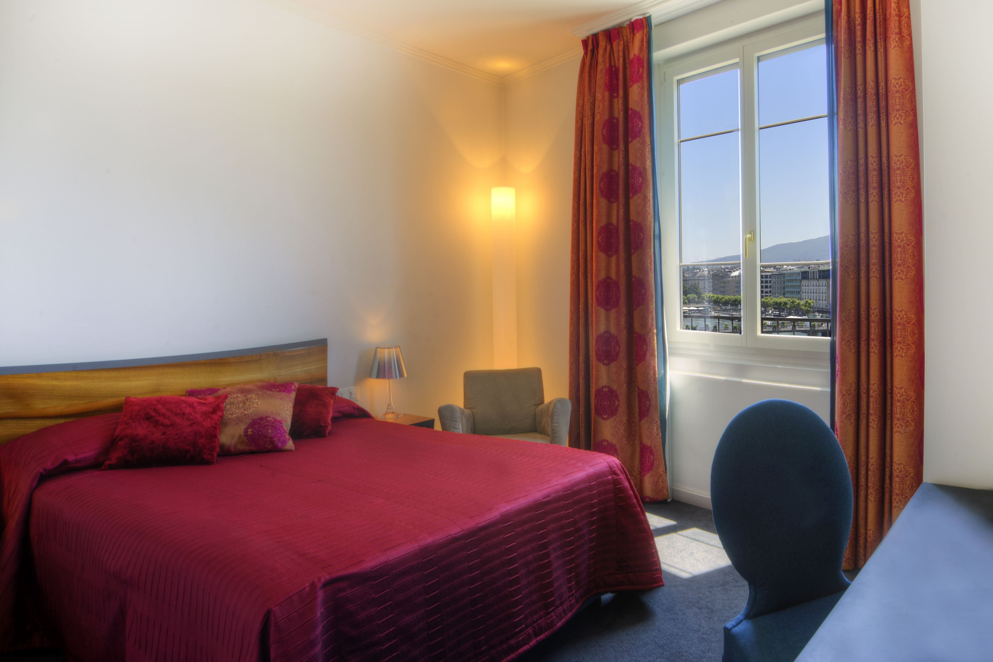 Une chambre d’hôtel avec un lit, une chaise, un bureau et une fenêtre avec des rideaux.