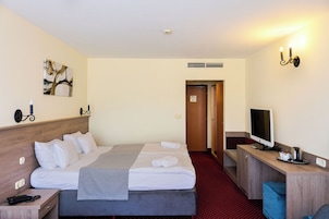 Quarto de hotel com cama, mesa de cabeceira, televisão e escrivaninha com cadeira.