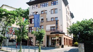 A hotel with a modern design, featuring a prominent balcony on the second floor and a flag on the facade.