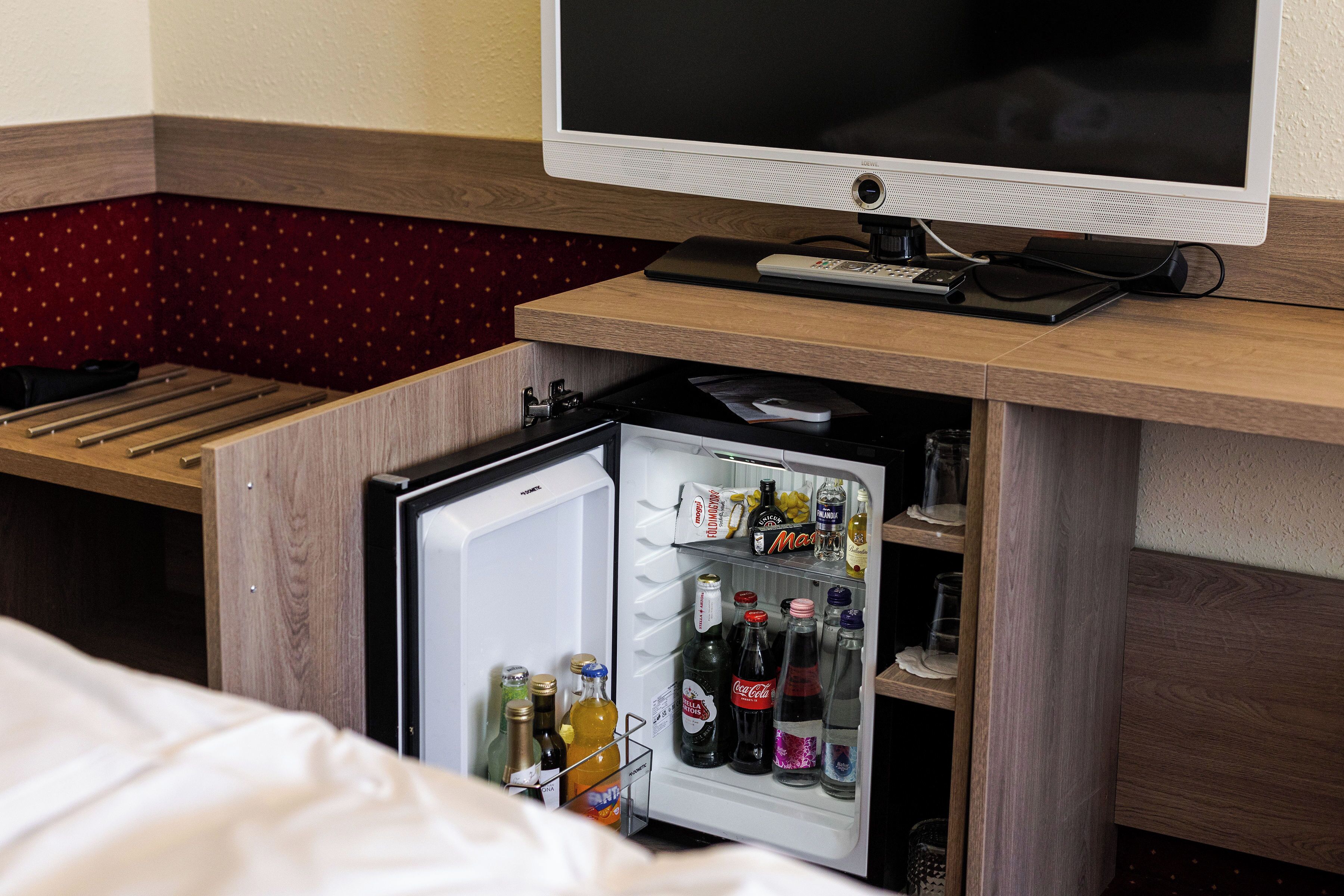 Habitación de hotel con cama, televisión y un mini refrigerador lleno de bebidas.