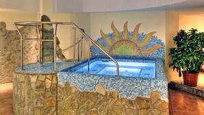 A hot tub with mosaic tiles, stone walls, and a metal staircase.
