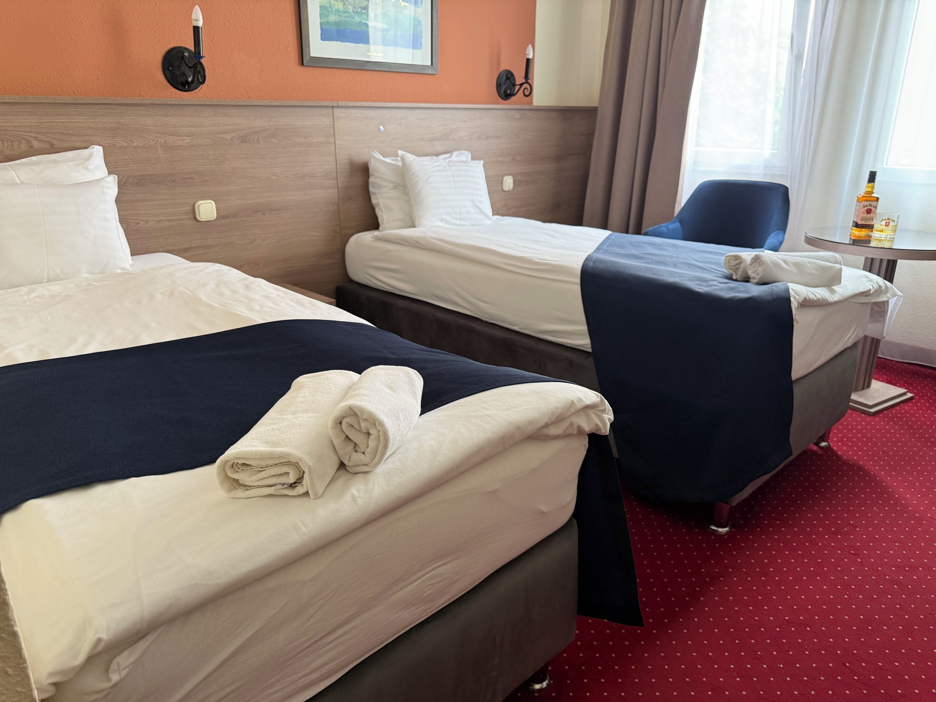 A hotel room with two beds, a desk, a chair, and a window with curtains.