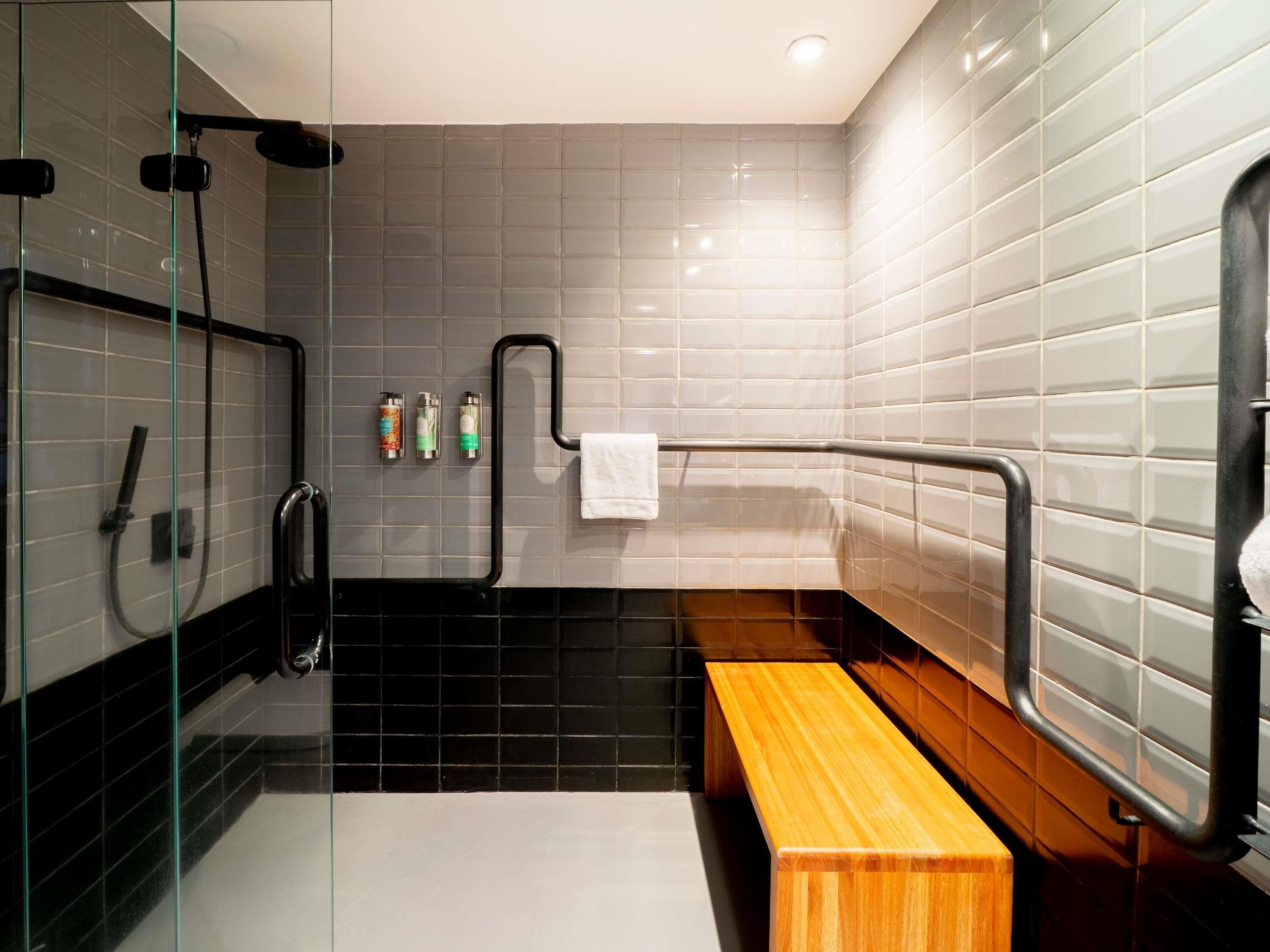 A modern bathroom with a glass shower enclosure, a wooden bench, and a towel rack.
