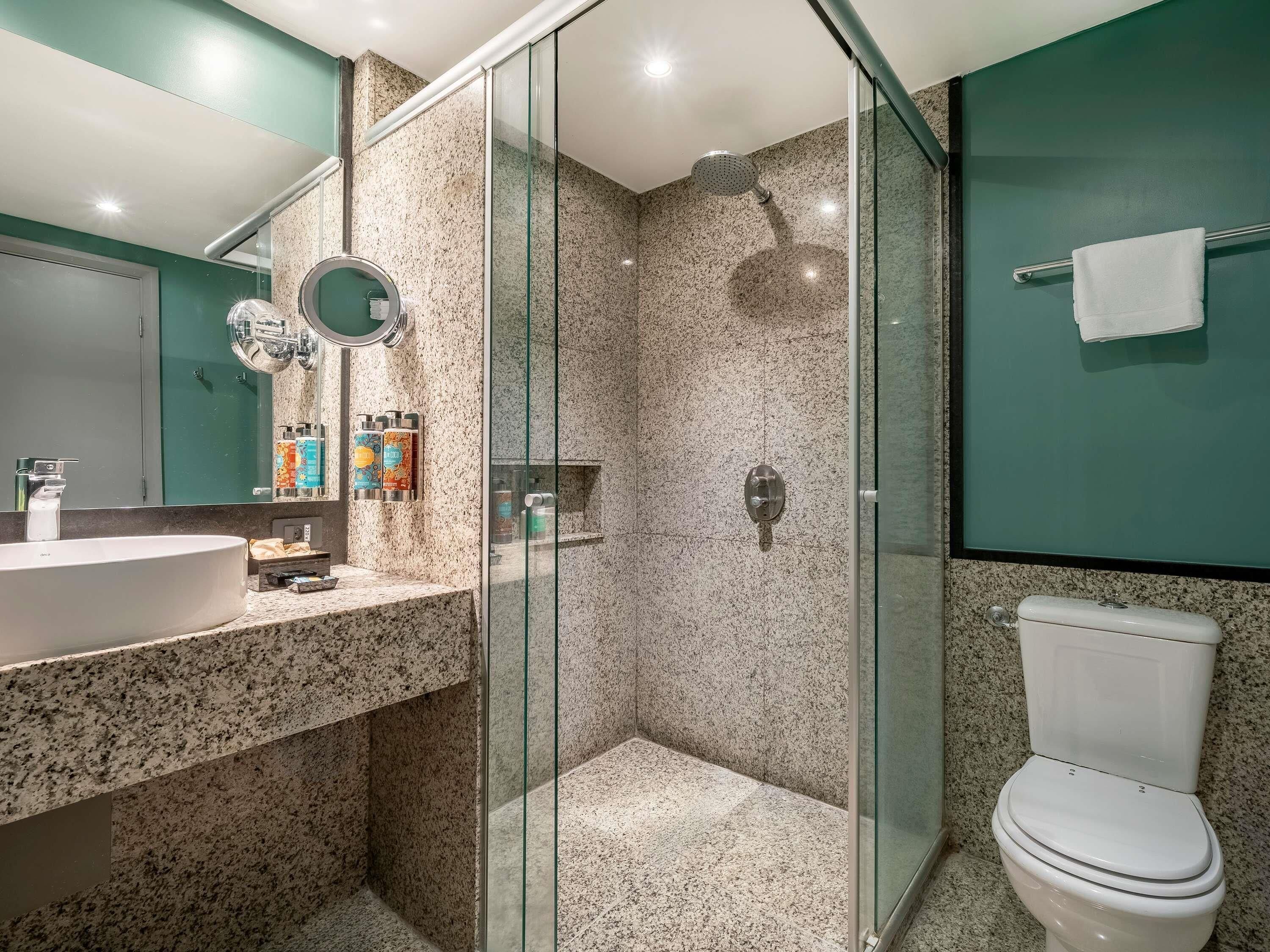 A modern bathroom with a granite countertop, a glass-enclosed shower, and a white toilet.
