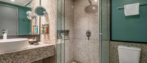 A modern bathroom with a granite countertop, a glass-enclosed shower, and a white toilet.