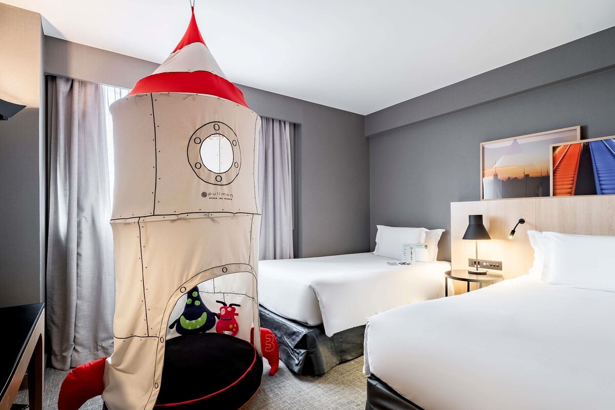 A hotel room with two beds, a pullman tent, and a nightstand with a lamp.