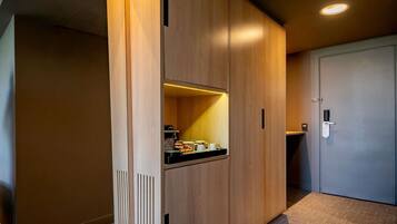Una habitación de hotel moderna con un armario de madera, una pequeña kitchenette y una puerta con cerradura digital.