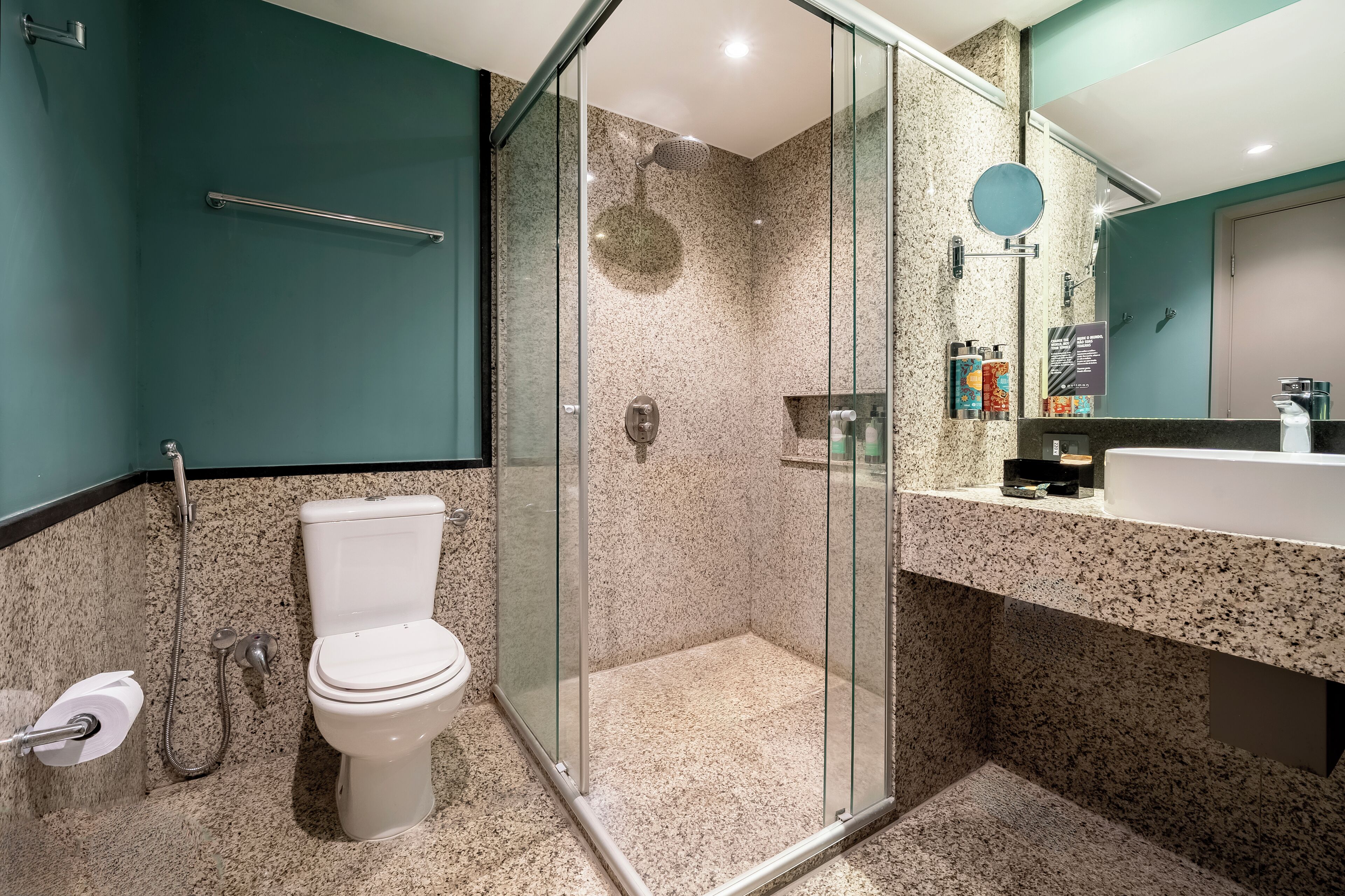 A modern bathroom with a glass-enclosed shower, a white toilet, and a granite countertop with toiletries.