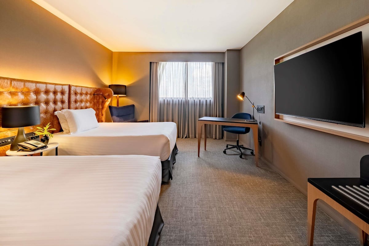 Habitación de hotel con dos camas, un escritorio, una silla, un televisor y una ventana con cortinas.