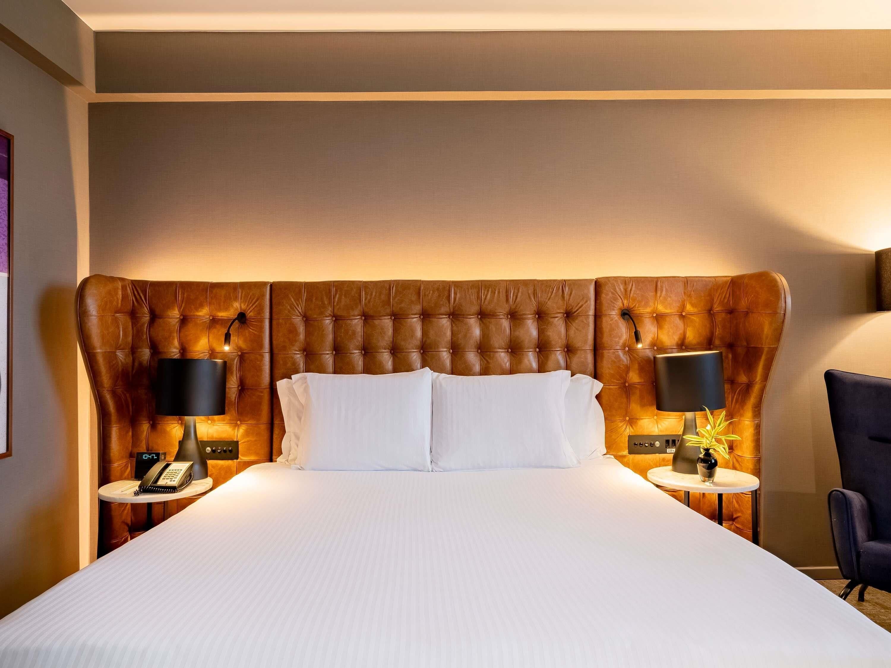 A hotel room with a large bed, two bedside tables with lamps, a clock, and a chair.