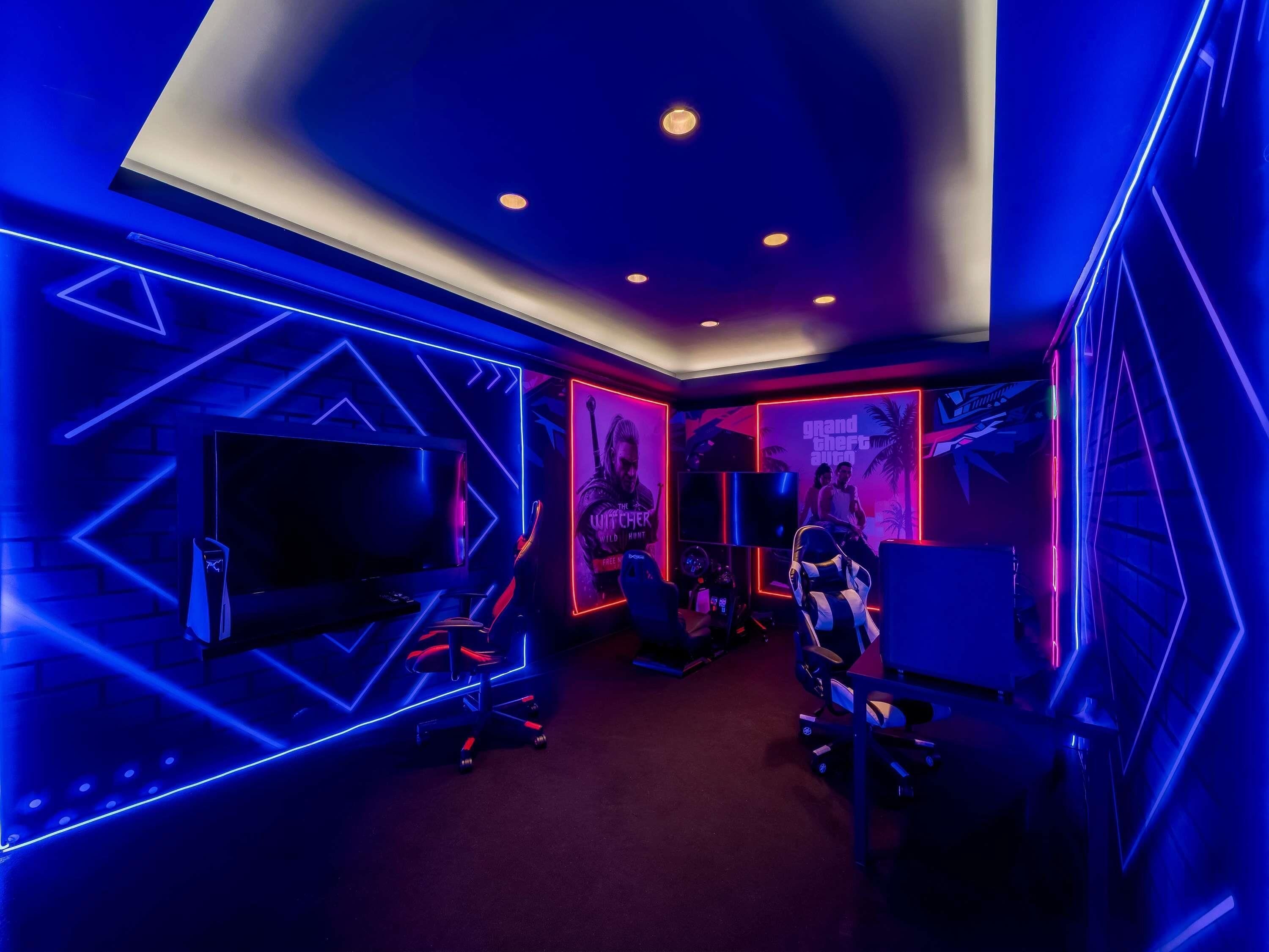 A room with a large flat-screen TV, gaming chairs, and a neon-lit wall with a 'Grand Theft Auto V' poster.