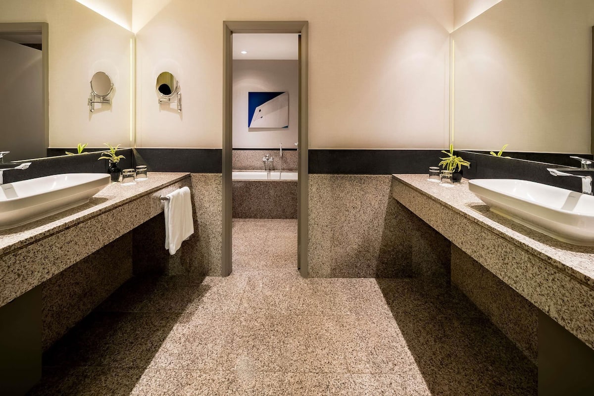 Un baño moderno con dos lavamanos, cada uno con un espejo y una toalla colgada en la pared. Hay una pequeña planta en la encimera del lavamanos de la izquierda.