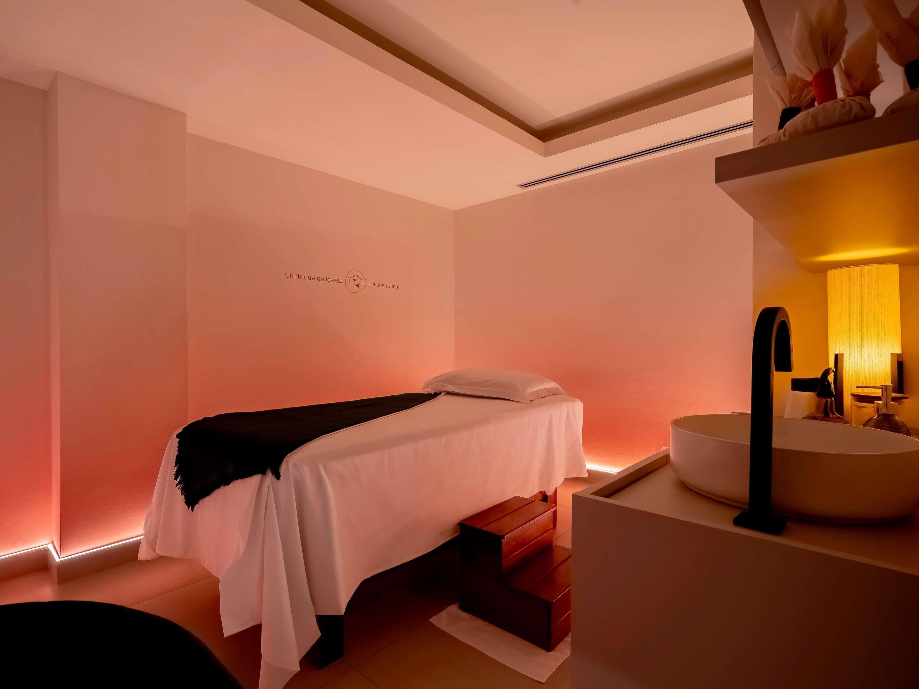 A hotel room with a bed, a bedside table, a sink, and a mirror.