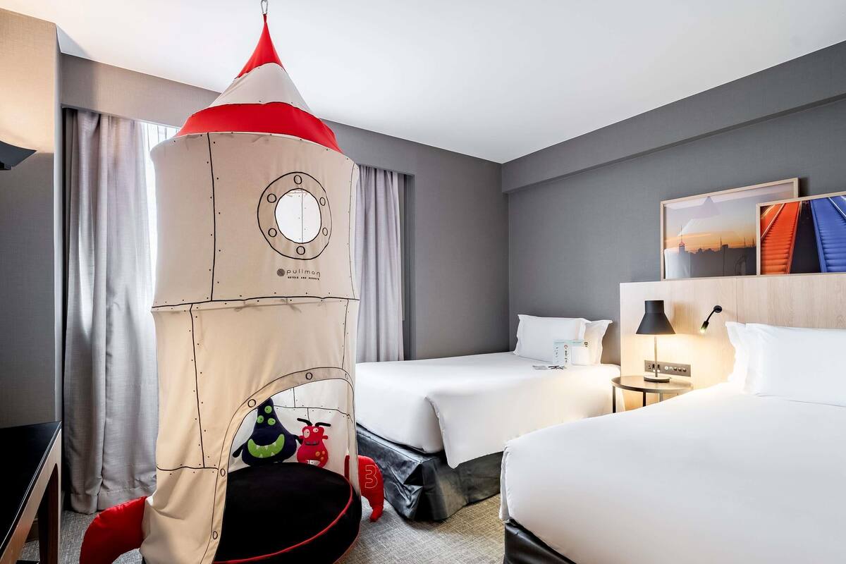 A hotel room with two beds, a pullman tent, and a nightstand with a lamp.