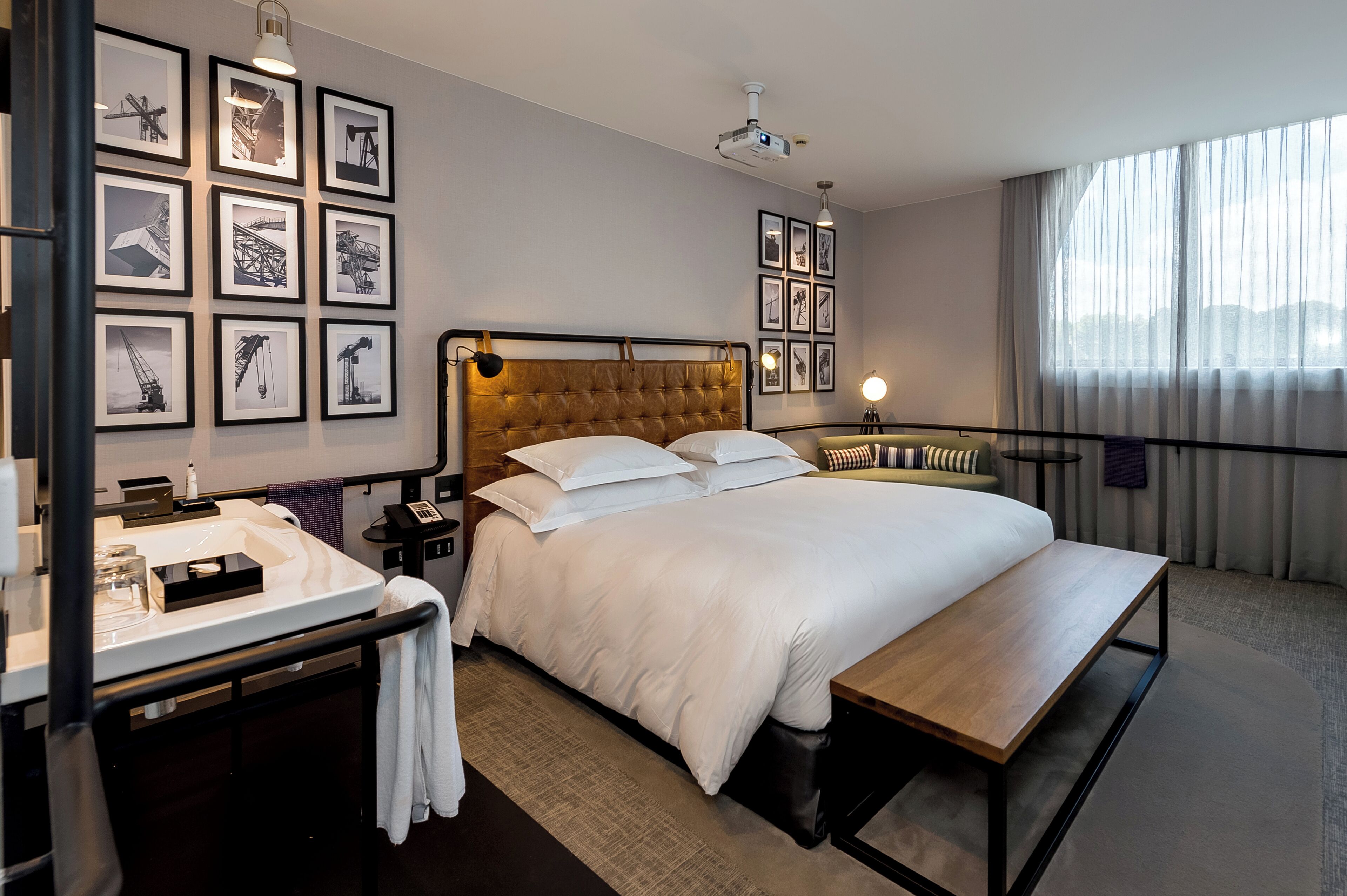 Habitación de hotel con una cama grande, una mesita de noche, un escritorio con teléfono y una pared decorada con cuadros.