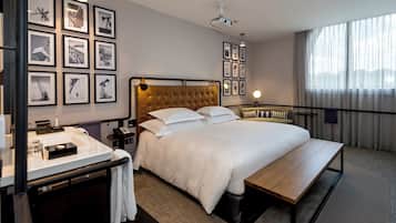 Habitación de hotel con una cama grande, una mesita de noche, un escritorio con teléfono y una pared decorada con cuadros.