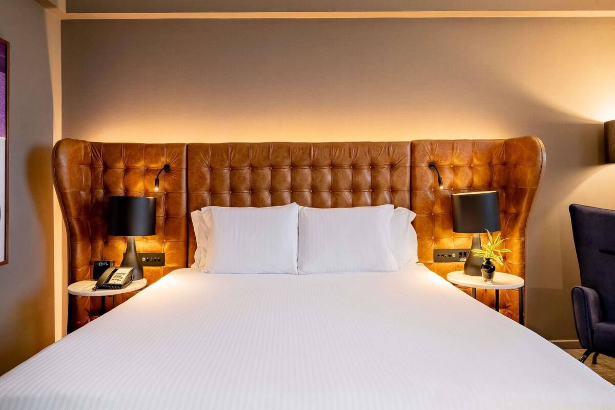 A hotel room with a large bed, two bedside tables with lamps, a clock, and a chair.