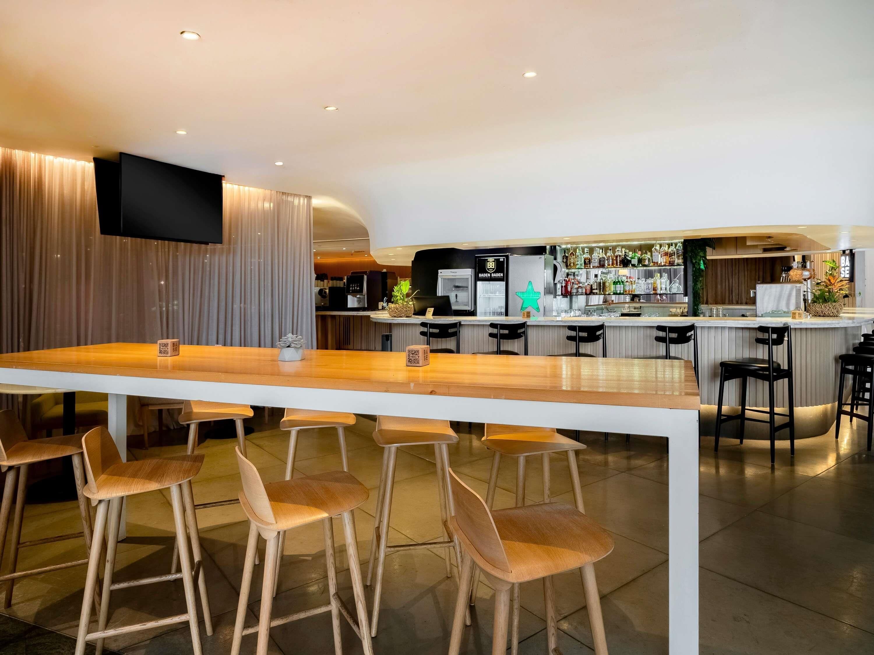 Zona de bar moderna con una barra larga, taburetes, un televisor de pantalla plana y una barra repleta de botellas.